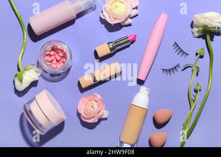 Set aus verschiedenen Kosmetika, Make-up Schwämmen und Ranunculus Blumen auf lila Hintergrund Stockfoto