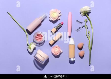 Set aus verschiedenen Kosmetika, Make-up Schwämmen und Ranunculus Blumen auf lila Hintergrund Stockfoto