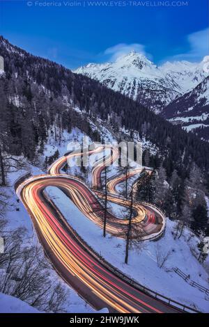 Lange Exposition mit leichten Wegen der Malojapassstraße in Engadin während der Blauen Stunde im Winter, Schweiz Stockfoto