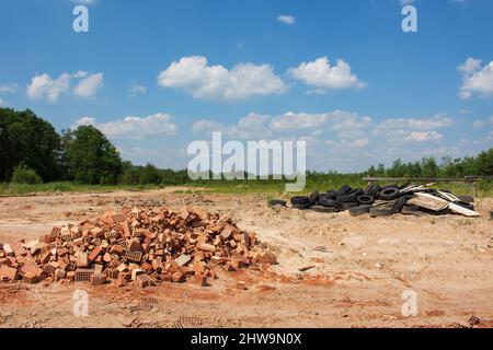 Umweltverschmutzung. Deponie von gebrochenen Ziegeln und gebrauchten Reifen in der Natur Stockfoto