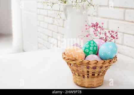 Bemalte bunte Ostereier im Korb mit Frühlingsblumen auf dem Tisch Stockfoto