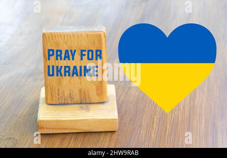 Beten Sie für die Ukraine Konzept - mit der Flagge der Ukraine in Form von Herzen auf Holzhintergrund. Stockfoto