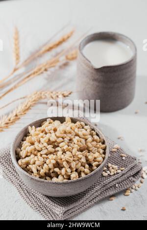 Schüssel mit gekochten geschälten Gerstenkörnern Haferbrei mit Ähren aus Weizen auf weißem Hintergrund. Kochen gesund und Ernährung Konzept. Stockfoto