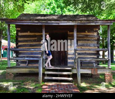 Die Blockhütte befindet sich auf dem Platz in Collierville, Tennessee. Die Hütte wurde Mitte des 19. Jahrhunderts als Etappenbus-Haltestelle genutzt. Attraktive junge Frau steht Stockfoto