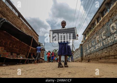 Ein junges Schulmädchen sah, wie es in Kibera eine Solaranlage auf der Straße trug. In den Slums von Kibera nutzen die meisten Bewohner, insbesondere Straßenhändler, private Schulen, Nichtregierungsorganisationen, Straßenlaternen und Schulen, das billige Solarenergiesystem, das eine zuverlässigere und billigere Energiequelle ist. Dies hat das Recycling der meisten von den Bewohnern verbrauchten elektrischen Energie etwas vereinfacht und auch dazu beigetragen, die hohe Zahl der Todesfälle durch Elektroschocks und die täglichen Slumbrände zu reduzieren. Stockfoto