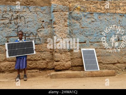 Ein junges Schulmädchen sah, wie es in Kibera eine Solaranlage auf der Straße trug. In den Slums von Kibera nutzen die meisten Bewohner, insbesondere Straßenhändler, private Schulen, Nichtregierungsorganisationen, Straßenlaternen und Schulen, das billige Solarenergiesystem, das eine zuverlässigere und billigere Energiequelle ist. Dies hat das Recycling der meisten von den Bewohnern verbrauchten elektrischen Energie etwas vereinfacht und auch dazu beigetragen, die hohe Zahl der Todesfälle durch Elektroschocks und die täglichen Slumbrände zu reduzieren. Stockfoto