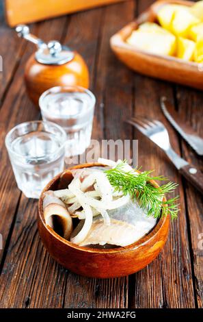 Schüssel mit gesalzenem Hering auf dem Hintergrund eines Glases Wodka und Dekanter. Gesalzener Hering im Glas als Snack für Wodka. Stockfoto