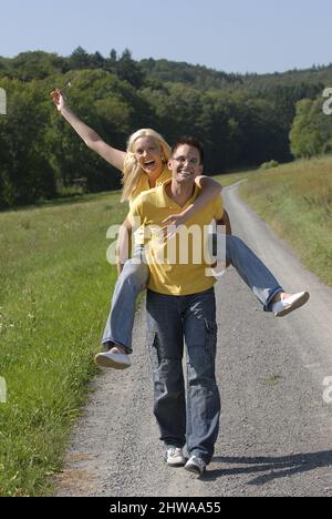 Mann, der eine Landstraße entlang läuft und seine Frau mit dem Huckepack trägt, Deutschland Stockfoto