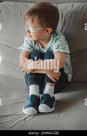 Kind mit Autismus in Brille sitzt auf dem Sofa und traurig Stockfoto