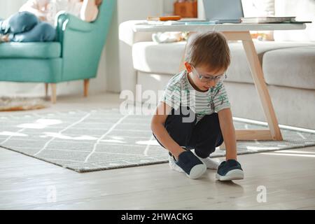 Ein Kind mit Autismus in einer Brille spielt mit seinen Schuhen Stockfoto