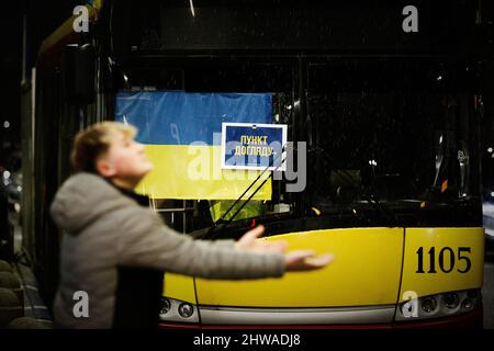 Am 04. März 2022 hält ein Mann während eines kurzen Hagelsturms vor einem Bus mit Versorgung für ukrainische Flüchtlinge und ukrainischer Flagge am Warschauer Ost-Bahnhof in Warschau, Polen, die Hände aus. Jeden Tag kommen mehrere tausend Flüchtlinge in den Warschauer Bahnhöfen an, die vor der Gewalt nach der Invasion Russlands fliehen. Fast eine Million Menschen sind nach der russischen Invasion aus der Ukraine geflohen, und rund 700 000 von ihnen sind nach Polen geflohen. Dank einer Reihe von privaten und öffentlichen Initiativen und den Bemühungen der lokalen Gemeinden wurden Flüchtlinge aus der Ukraine mit offenen Waffen und en aufgenommen Stockfoto