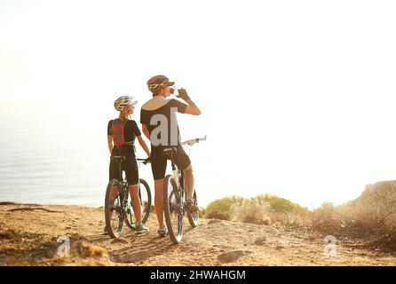 Kommen Sie der Natur näher. Aufnahme eines jungen Paares, das während einer Radtour die Aussicht von einem Hügel aus bewundert. Stockfoto