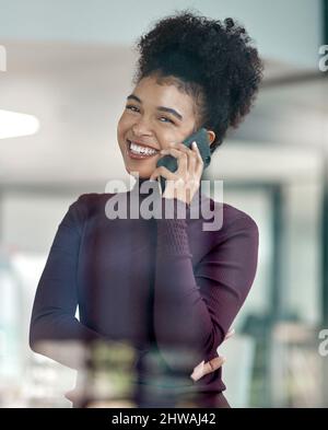 Aufnahme einer selbstbewussten jungen Frau, die ihr Mobiltelefon bei der Arbeit benutzt. Aufnahme einer selbstbewussten jungen Frau, die ihr Mobiltelefon bei der Arbeit benutzte und mit ihrem Arm lächelte Stockfoto