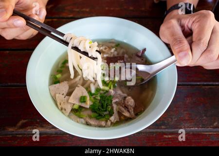 Vietnamesisches Essen, Reisnudeln, Pho Bo vietnamesische Suppe mit Rindfleisch und Essstäbchen in männlicher Hand im Restaurant von thailand Stockfoto