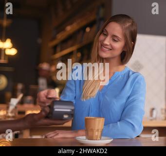 Die Bezahlung war noch nie einfacher. Kurzer Schuss einer attraktiven jungen Frau, die in einem Café bezahlt. Stockfoto