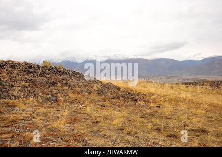 Blick von der Spitze eines felsigen Hügels auf die trockene Wüstensteppe am Fuße der schneebedeckten Berge. Kurai-Steppe, Altai, Sibirien, Russland. Stockfoto