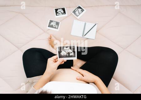 Eine nette Schwangeren Bauch und Röntgen-Ultraschall-Scan des Babys. asiatische junge schwanger Frau entspannen sich im Zimmer Blick auf ihr Kind Bild in den Händen süß. Mo Stockfoto