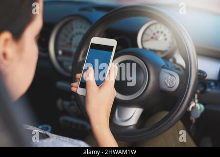 Abgelenkt fahren. Aufnahme einer Frau, die während der Fahrt ein Telefon benutzt. Stockfoto