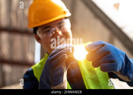 Asian glücklich Elektriker mit Glühbirnen und die Festsetzung des Lichts im Inneren renovierte Wohnung in Baustelle. Stockfoto