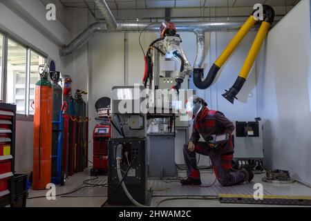 Ein Ingenieur oder Arbeiter trägt eine Sicherheitsmaske steuern den intelligenten Roboter Schweißen Handsystem automatisierte Fertigung Maschine Motor in der Fabrik, Stockfoto