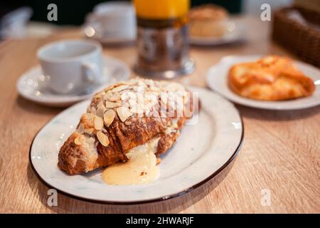 Ein frisches großes Croissant auf einem schönen Teller in einem Café oder Restaurant. Nahaufnahme eines Croissants und einer mit Nüssen bestreuten Creme. Süßes und köstliches Dessin Stockfoto