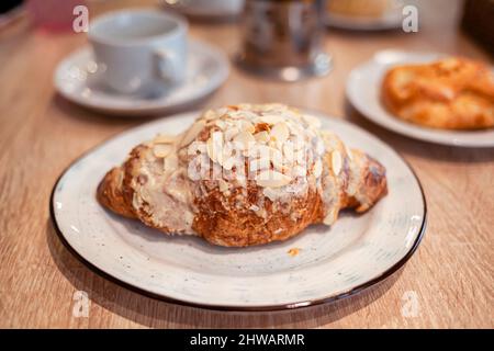 Ein frisches großes Croissant auf einem schönen Teller in einem Café oder Restaurant. Nahaufnahme eines Croissants und einer mit Nüssen bestreuten Creme. Süßes und köstliches Dessin Stockfoto