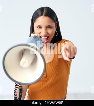 Wir brauchen Ihre Unterstützung. Beschnittenes Porträt einer attraktiven jungen Frau, die in ein Megaphon schreit und im Studio auf die Kamera zeigt. Stockfoto