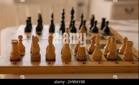 Hölzerne Schachfiguren stehen in einer Reihe auf einem alten Schachbrett Anfang des Spiels. Stockfoto