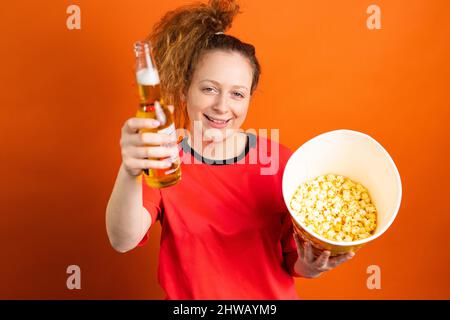 Fußballfan jubelt und unterstützt ihre Fußballmannschaft mit einer Flasche Bier und Popcorn in den Händen. Stockfoto