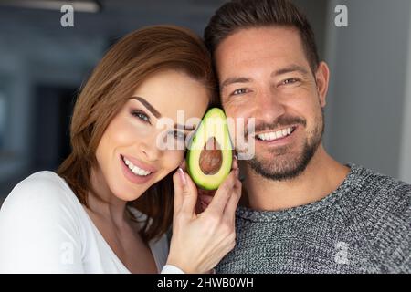 Glückliches junges kaukasisches Paar mit Avocado im Gesicht Porträt Stockfoto