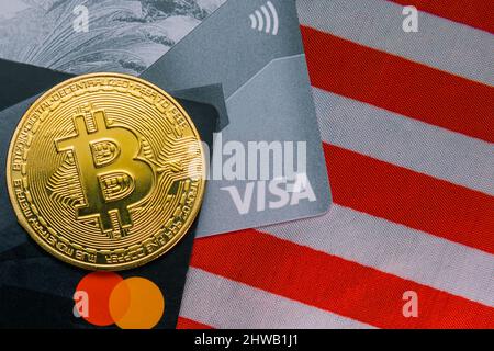 Die Bitcoin-Münze liegt auf Bankkarten mit VISA- und MasterCard-Zahlungssystemen. Unter ihnen ist die Flagge der Vereinigten Staaten. BTC-Kryptowährung. Schließen Stockfoto