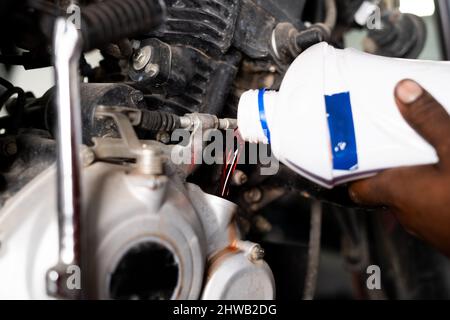 Nahaufnahme der mechanischen Hände, die Öl in den Motor in der Garage gießen - Konzept des Motorwartungsservice und der Motorschmierung. Stockfoto