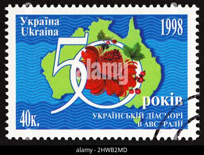 UKRAINE - UM 1998: Eine in der Ukraine gedruckte Briefmarke, die zum 50.. Jahrestag der Ukrainer in Australien ausgegeben wurde, zeigt eine Karte von Australien und Waratah. Stockfoto