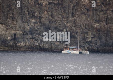 Los Cristianos, 24. Oktober 2021: Touristenkatamaran neben einer Klippe. Guaza Mountain Natural Monument. Arona. Teneriffa. Kanarische Inseln. Spanien. Stockfoto