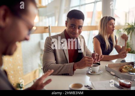 Der junge Geschäftsmann hat sich während einer Mittagspause in angenehmer Atmosphäre am Tisch im Firmengebäude gut Vergnügen und genießt ein Stockfoto
