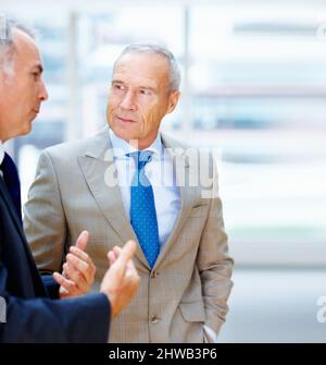 Zwei Führungskräfte unterhalten sich. Zwei hochrangige Geschäftsleute, die in Innenräumen diskutieren. Stockfoto