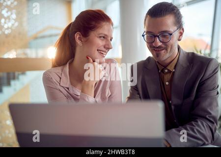 Zwei junge Geschäftskollegen in freundlicher Atmosphäre im Büro haben eine gute Zeit, während sie zusammen einen Laptop-Inhalt genießen. Unternehmen, Menschen, von Stockfoto