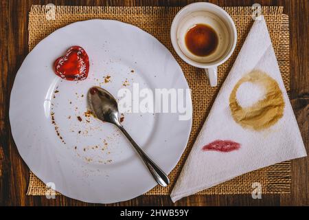 Was bleibt von einem Frühstück, das von einer Frau gegessen wurde, die Lippenstiftflecken und andere Flecken auf einer Papierserviette und Krümel auf ihrem Teller hinterließ Stockfoto