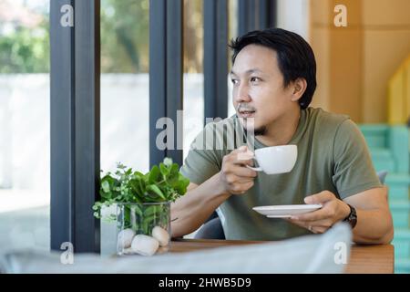 Asiatischer Geschäftsmann, der in einem modernen Café oder Büro neben dem Glas trinkt und von zu Hause aus arbeitet, fühlt sich glücklich an seinem Schreibtisch, Geschäftsinhaber und Entr Stockfoto