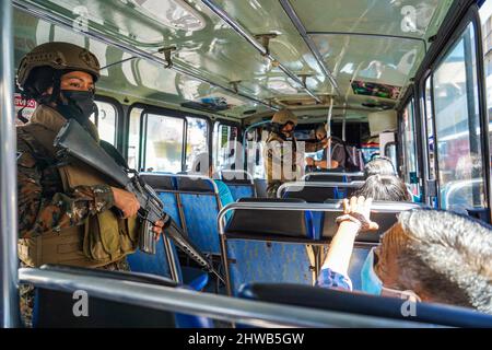 San Salvador, El Salvador. 04. März 2022. Während einer Militärpatrouille in der Innenstadt von San Salvador bewacht eine Soldatin einen Bus. Seit 2000 dürfen Frauen die Reihen der salvadorianischen Streitkräfte integrieren, am 8.. März wird der Internationale Frauentag gefeiert, wobei die Öffnung traditioneller, von Männern geführte Räume für Frauen eine von vielen Forderungen ist. Kredit: SOPA Images Limited/Alamy Live Nachrichten Stockfoto