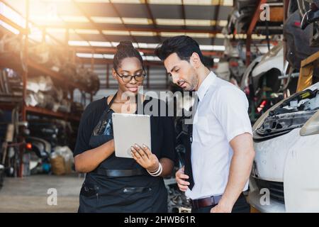 Afrikanische Frau, die im alten Teil der Autofabrik arbeitet und auf dem Tablet nachschaut und mit dem Chef oder Kunden spricht Stockfoto