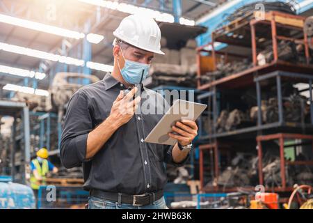 Inspektor Vorarbeiter mit Gesichtsmaske oder Ingenieur Manager Blick auf Tablet und Kontrolle der Arbeit per Funk in der Fabrik Stockfoto