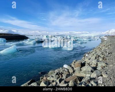 Eisige Küstenlandschaft an einem isländischen Ufer, voll von großen Eisstücken am Strand und schwimmend im Wasser. Stockfoto