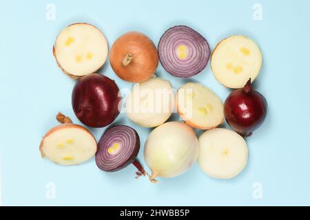 Drei Zwiebelzwiebeln in verschiedenen Farben (rot, gelb und weiß) isoliert auf blauem Hintergrund. Hochauflösendes Foto. Volle Schärfentiefe. Stockfoto