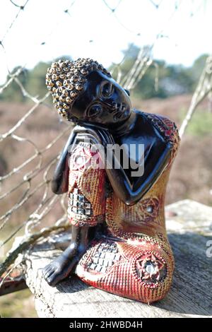 Verträumte dekorative Buddha sitzt auf einer Bank draußen. Stockfoto