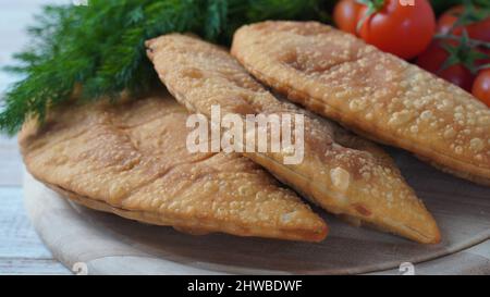 Cheburek mit Fleisch und Kirschtomaten. Traditionelle rumänische, ukrainische, russische und tatarische Küche Nationale Ostmahlzeit. Fleischpastete mit Rind, Kalb oder Lamm Stockfoto