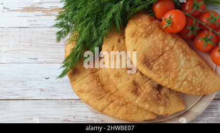 Cheburek mit Fleisch und Kirschtomaten. Traditionelle rumänische, ukrainische, russische und tatarische Küche Nationale Ostmahlzeit. Fleischpastete mit Rind, Kalb oder Lamm Stockfoto