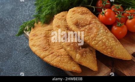 Cheburek mit Fleisch und Kirschtomaten. Traditionelle rumänische, ukrainische, russische und tatarische Küche Nationale Ostmahlzeit. Fleischpastete mit Rind, Kalb oder Lamm Stockfoto