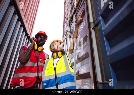 Zwei afroamerikanische Arbeiter mit Funkkommunikation und Kontrolle der Verladung von Frachtschiffen vom Frachtschiff auf Impo Stockfoto