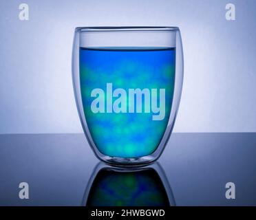 Doppelwandiger isolierter Glasbecher, gefüllt mit blauer und grüner Flüssigkeit und rundem Eis.heller reflektierender Hintergrund Stockfoto